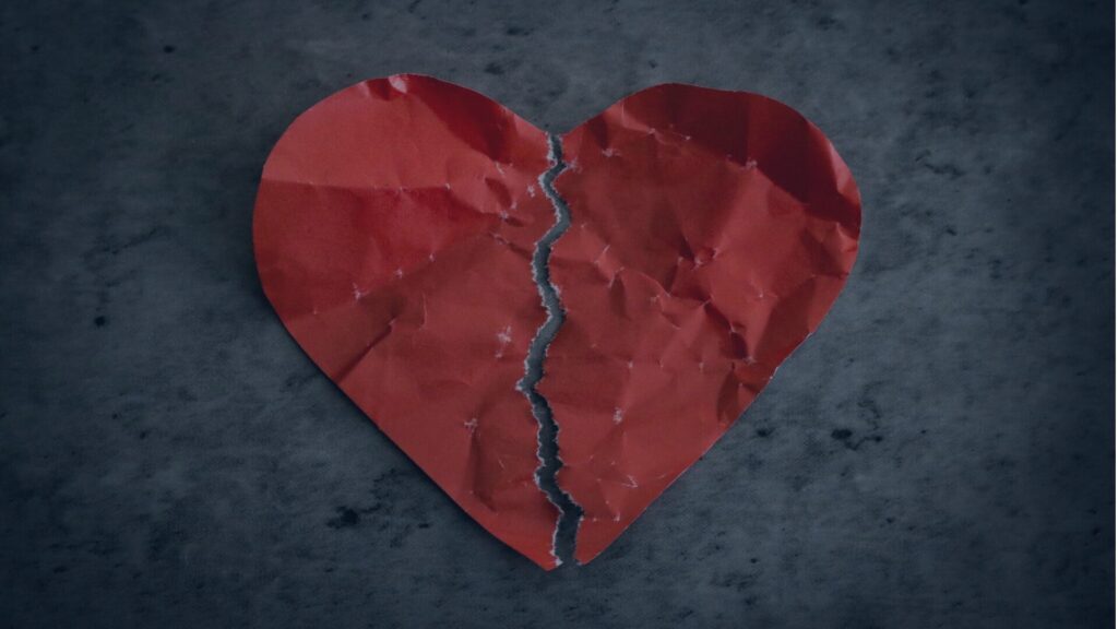 Crumpled red heart symbolising heartbreak and emotional harm from romance scams.