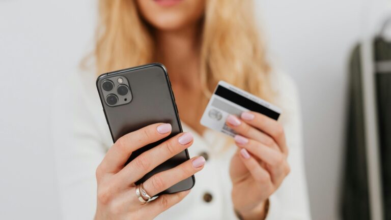Woman holding phone and bank card, a common moment targeted by OTP fraud scams in the UK